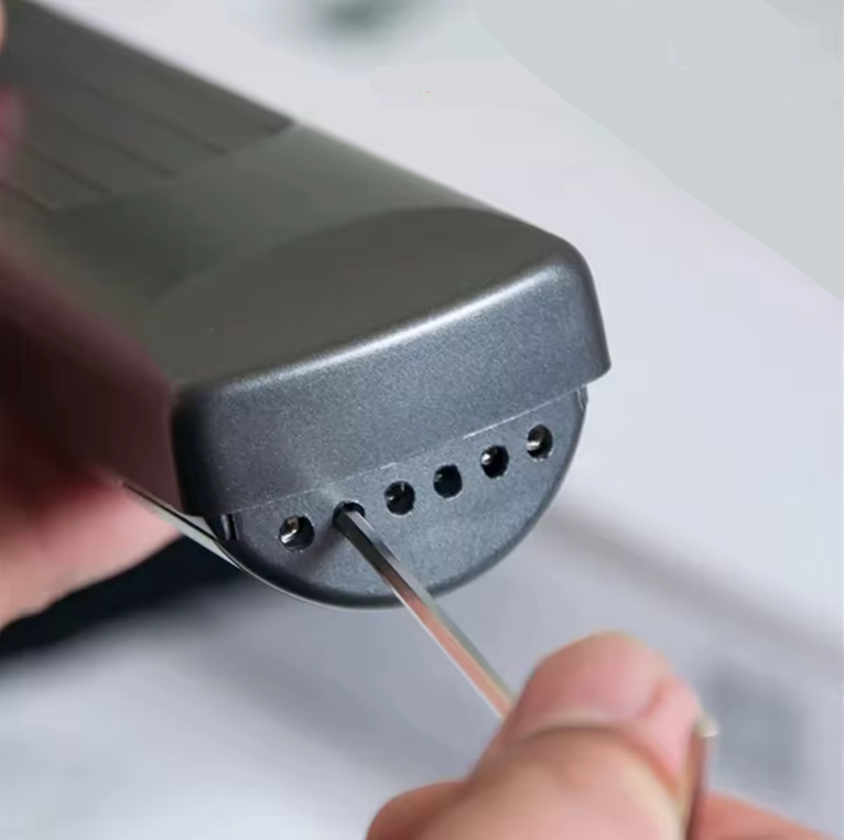 Person adjusting the strings of a guitar training device with an Allen Key on a light background