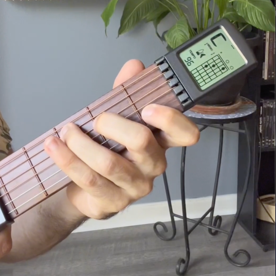 Hand playing a guitar trainer with a digital chord screen