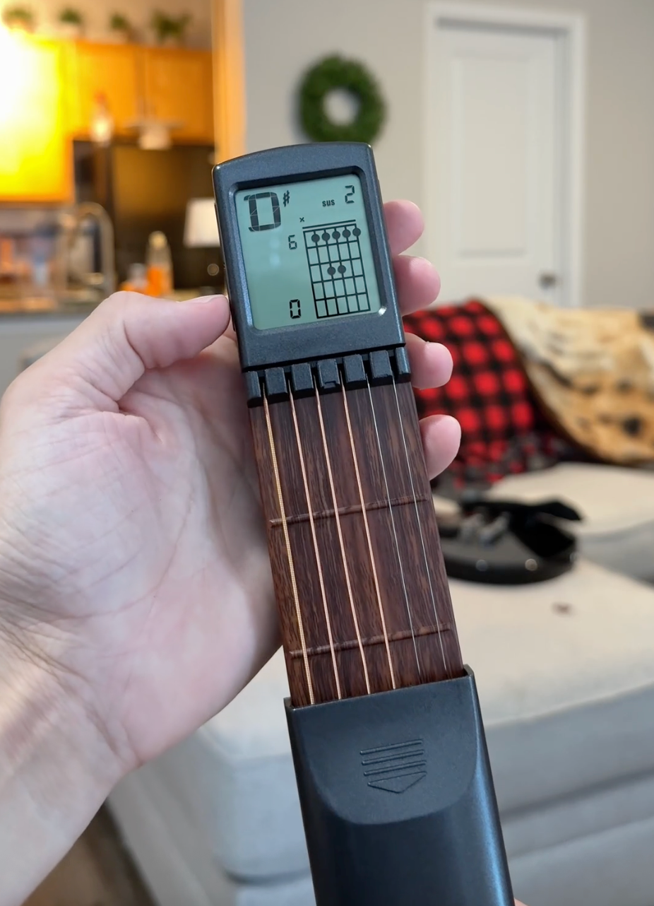 Guitar with a digital chord display held by a hand in a home setting
